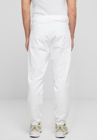 Pantalones de mezclilla blancos con un diseño de corte recto, dos bolsillos traseros y una cinturilla. Combinados con zapatillas deportivas beige. Textura suave.