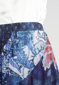 En mönstrad kjol med blått och blommigt motiv, med en texturerad midjeresår och tyg som övergår från enfärgad till tryckt.