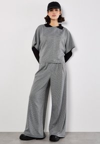 Grårutig tvådelad outfit med en avslappnad topp med svart krage och vida byxor. Bärs med en svart keps och klumpiga skor.