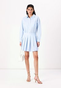 Vestido camisa azul claro, listrado, com mangas longas, fecho botão na frente, dois bolsos no peito, cintura ajustada, saia rodada, combinado com sandálias de tiras.
