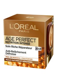 Boîte de crème L'Oréal Age Perfect, dorée et brune avec un motif en nid d'abeille, présente un texte en blanc et noir, ainsi qu'une petite fenêtre transparente.