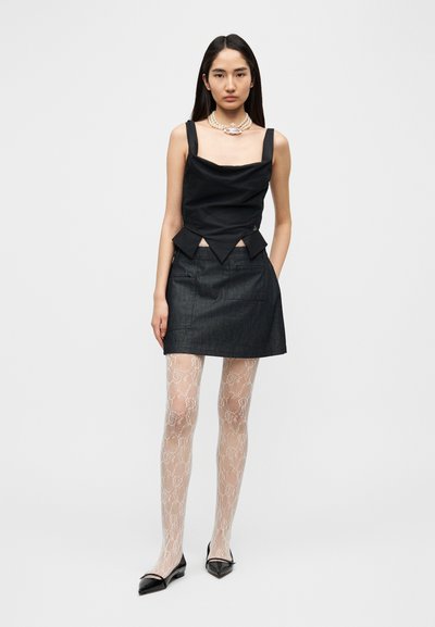 Μαύρο τοπ από ύφασμα με λαιμόκοψη τύπου κουκούλα και τριγωνική χαμηλή γραμμή, σε συνδυασμό με σκούρα τζιν φούστα. Λευκές καλσόν με σχέδια και μαύρα μυτερά παπούτσια.