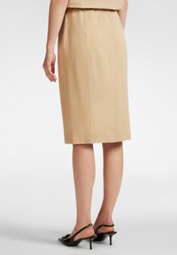 Gonna a tubino beige con design aderente, cintura elastica e taglio al ginocchio. Indossata con sandali neri con tacco. Tessuto liscio.