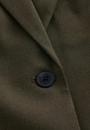 Olivengrønt stof på en jakkekrave med en sort knap med fire huller; glat tekstur og skarpe reverskanter.