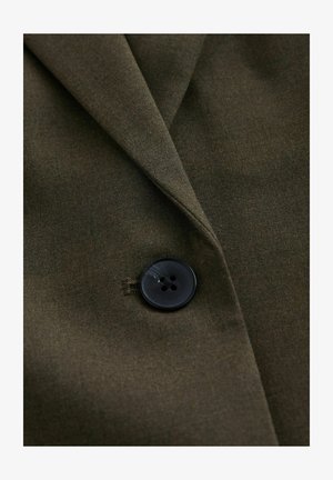 Olivengrønt stof på en jakkekrave med en sort knap med fire huller; glat tekstur og skarpe reverskanter.