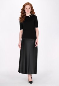 Top negru cu mâneci scurte și dublu alb, asortat cu o fustă lungă din satin negru. Look-ul este completat cu tocuri înalte negre.