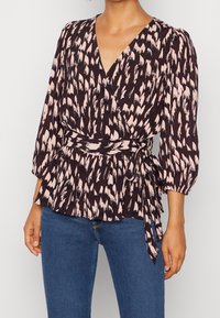 Schwarz-pink gemusterte Bluse mit V-Ausschnitt, Ballonärmeln und gebundenem Taillengürtel. Der Stoff hat eine weiche Textur und ein Peplum-Design.
