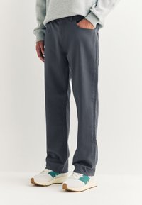 Szare bawełniane spodnie o prostym kroju, z bocznymi kieszeniami i prostym designem; zestawione z białymi trampkami z zielonymi akcentami.