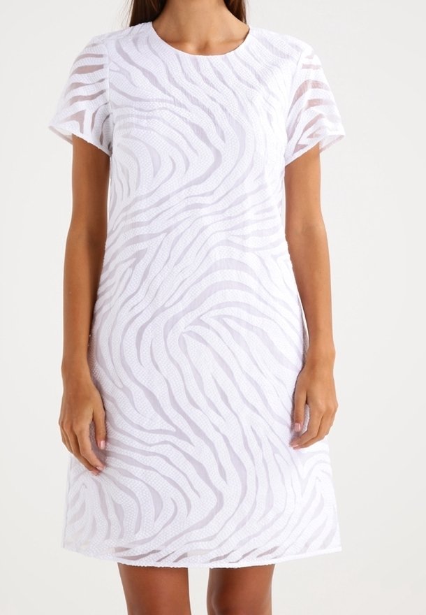 Femme portant une robe blanche à manches courtes, longueur genou, avec un motif zébré transparent.