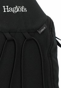 Zaino nero con logo "Haglöfs" in bianco. Presenta cinghie elastiche e un'etichetta con scritto "Corker Jr." realizzata in tessuto resistente.
