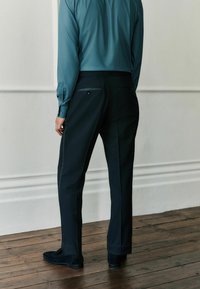 Čierne nohavice s rovnými nohavicami, so zadnými vreckami, kombinované s tmavočiernou košeľou na gombíky a zamatovou obuvou.