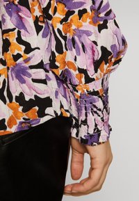 Blusa con motivo floreale nei toni di lilla, arancione e nero. Presenta polsini elasticizzati, tessuto testurizzato e una vestibilità rilassata. Accenti in pelle nera all'orlo.