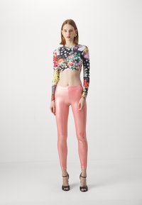 Kvetinový crop top s dlhými rukávmi v kombinácii farieb; lesklé ružové legíny; čierne sandále na vysokom opätku; hladké textúry.