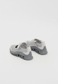 Scarpe da ginnastica grigie e grigie chiare con tomaia in rete, cinturino regolabile, suola ammortizzata e un design con fori distintivi sul fondo.