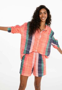 Pruhovaný set trička a šortiek v koralovej, modrej a zelenej farbe. Voľne strihané tričko s krátkym rukávom má gombíky; šortky s elastickým pásom. Zmiešaný bavlnený materiál.