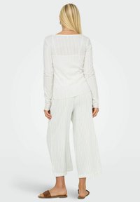 Haut à manches longues blanc côtelé associé à un pantalon large à rayures claires et des sandales plates marron, mettant en avant un style décontracté et confortable.