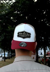 Lkw-Fahrer-Kappe mit einer weißen Vorderseite, bordeauxrotem Schirm und Netzrücken. Sie verfügt über ein schwarz-weißes gesticktes Logo mit "New Era Cap Company".