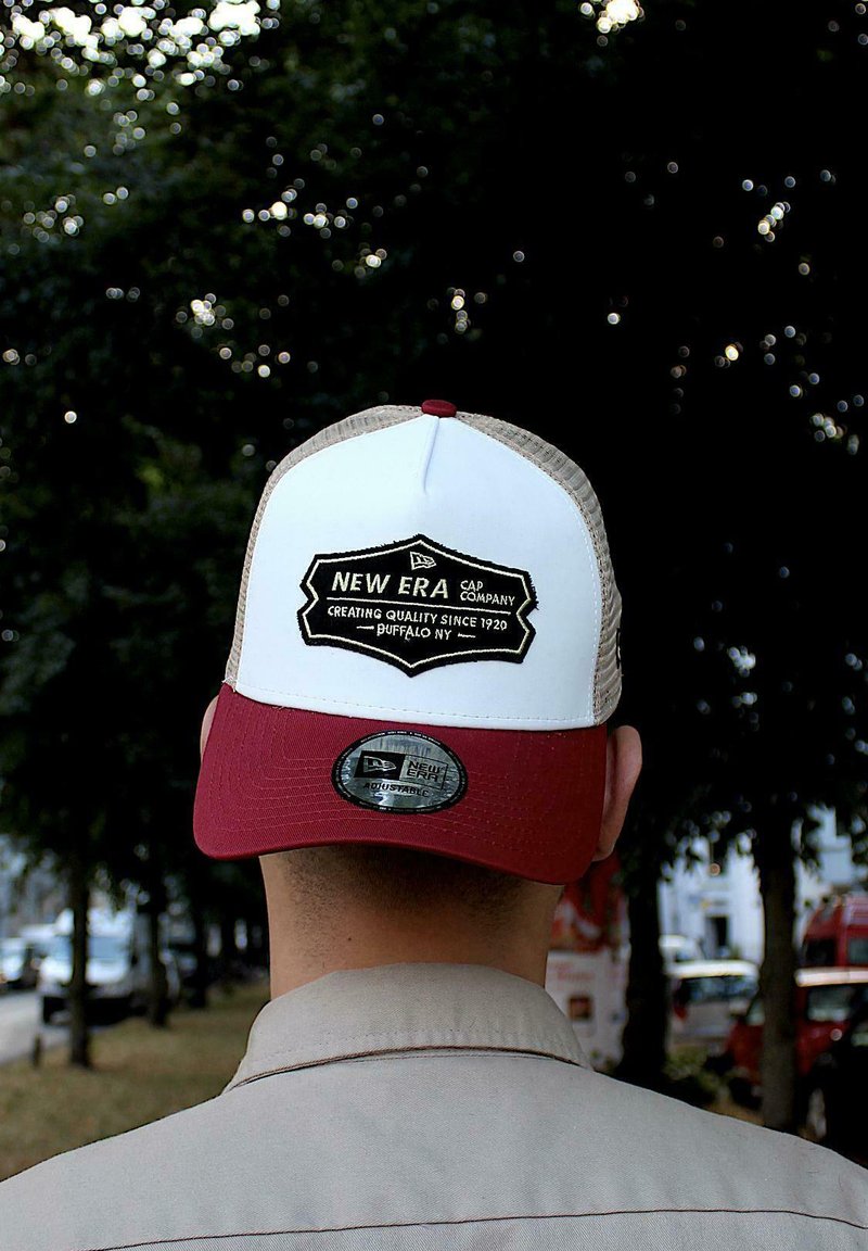 Lkw-Fahrer-Kappe mit einer weißen Vorderseite, bordeauxrotem Schirm und Netzrücken. Sie verfügt über ein schwarz-weißes gesticktes Logo mit "New Era Cap Company".
