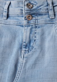 Tela de denim azul claro con una textura suave, con dos botones de metal plateado en la cintura y detalles de costura visibles.