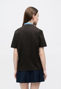 Pruun, lühikeste varrukatega T-särk, helesinise kraega, valmistatud pehmest kangast. Särk on lõdva istuvusega ega sisalda nähtavaid mustreid.