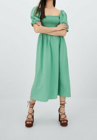 Mint vihreä, puolipitkä mekko puffhihoilla ja smocked-rintakappaleella. Yhdistetty ruskeisiin platform-sandaaleihin, joissa on nauhanaulittavat hihnat. Muotoiltu kangas.