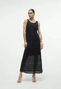 Vestido preto longo com um design de malha aberta, corte sem mangas e silhueta reta. Textura suave com um padrão em camadas.