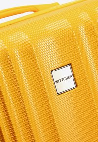 Geel harde koffer met een honingraatstructuur, voorzien van een metalen logoplaat met de tekst "WITTCHEN" aan de voorkant.