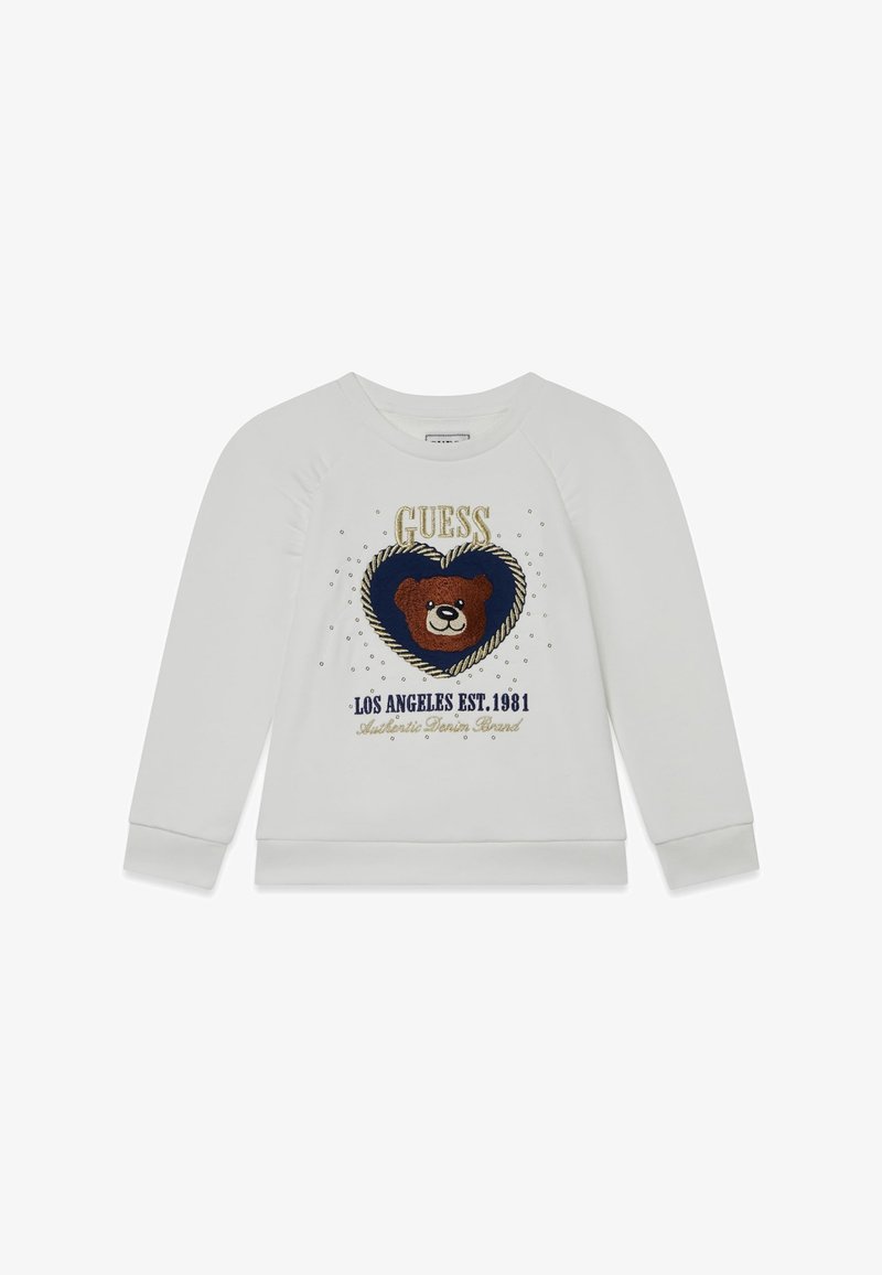 Pull blanc à manches longues avec un ours en peluche à l'intérieur d'un cœur bleu marine, entouré de petits points et du texte "GUESS Los Angeles Est. 1981".