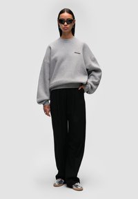 Felpa grigia oversize con scollo a girocollo, abbinata a pantaloni neri a gamba larga e scarpe argento. Occhiali da sole neri completano il look.