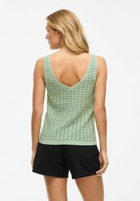 Canottiera in maglia verde menta con un design testurizzato e pattern, caratterizzata da uno scollo a V profondo e spalline larghe, abbinata a pantaloni corti neri.