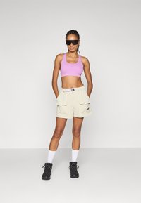 Lys grå cargo shorts med to frontlommer, kombinert med en tettsittende lilla sports-bh. Outfitten fullføres med svarte snøringer støvler og hvite sokker.