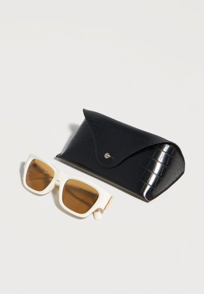 Γυαλιά ηλίου με λευκό πλαίσιο και καφέ φακούς δίπλα σε μαύρη υφασμάτινη σκληρή θήκη με κούμπωμα σε λευκό φόντο.