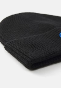 Zwarte gebreide beanie met een geribbelde textuur, met een blauw logo. De omslag is iets omgevouwen, waardoor een zachte, warme stof zichtbaar is.