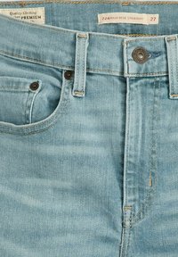 Jeans de mezclilla de color azul claro con corte recto de cintura alta. Las características incluyen un bolsillo delantero, cierre de botón metálico y costuras en contraste. Etiqueta de tamaño visible.