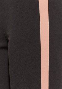 Svarta leggings med en vertikal pastelrosa rand längs sidan. Materialet verkar vara stretchigt med en mjuk textur.