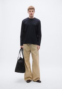 Črna majica z dolgimi rokavi z okroglim izrezom in grbom, bež široke hlače in črna torbica z vzmetjo in podrobnostmi z zadrgo.