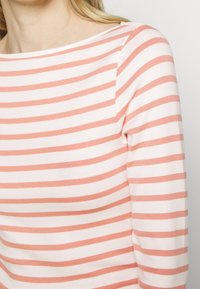 Lätt långärmad topp med båturringning och växlande korall- och vita horisontella ränder samt en mjuk och slät yta.
