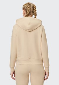 Hooded sweatshirt in light beige, featuring a soft texture, ribbed cuffs, and a small logo detail near the waist. Simple and relaxed fit.