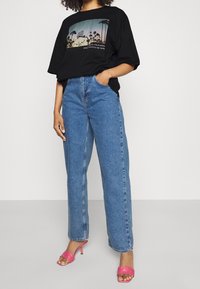 Czarny, oversize'owy T-shirt z grafiką palmy, niebieskie dżinsy z wysokim stanem i różowe sandały na obcasie. Casualowa stylizacja o luźnym kroju.