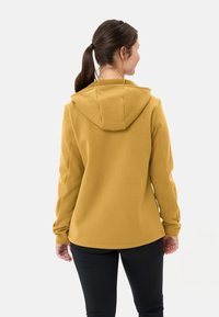 Geel hoodie met een buidelzak, verstelbare capuchon en een zachte, gestructureerde stof. Gecombineerd met zwarte leggings voor een casual look.
