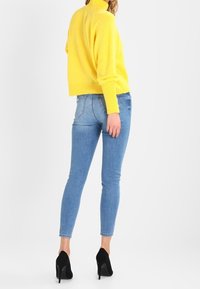 Yellow knitted turtleneck, cropped design, paired with light blue skinny jeans and black high-heeled shoes, with smooth textures.