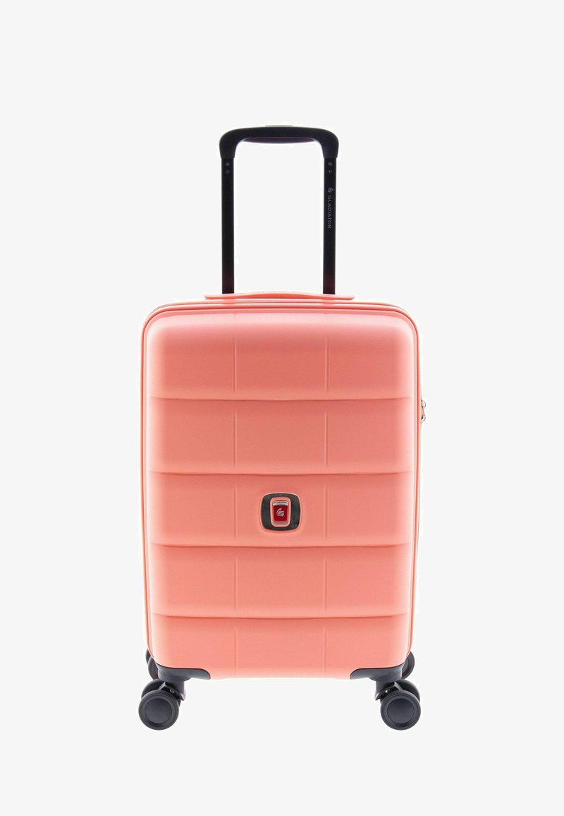 Valise rigide de couleur corail, avec une surface texturée à lignes horizontales, une fermeture éclair centrale et une poignée noire rétractable. Quatre roues.