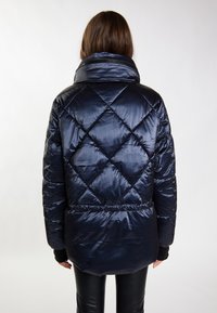 Giacca puffer blu navy con motivo a diamante trapuntato, colletto alto e vita elastica. Texture liscia e lucida, adatta per il clima freddo.