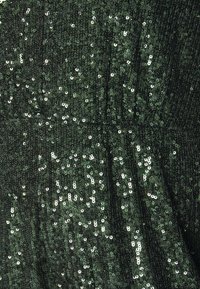 Tissu vert foncé densément couvert de sequins brillants reflétant la lumière dans un motif texturé et froncé.