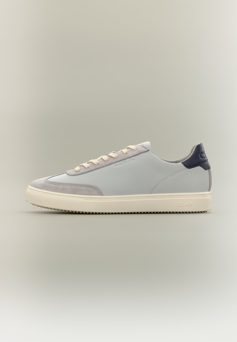 Χαμηλής κοπής καθημερινό αθλητικό παπούτσι με ανοιχτό γκρι δέρμα και επάνω μέρος από σουέτ, κορδόνια και σόλα σε κρεμ απόχρωση, και σκουρόχρωμη γλώσσα φτέρνας με τη σήμανση "CLAE".