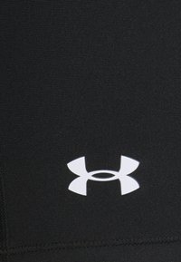 Białe logo Under Armour na czarnym teksturowanym tle, wyśrodkowane w dolnej części widocznego obszaru tkaniny.