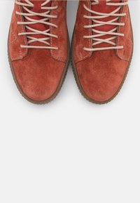 Mockasinsknä boots i djup orange med beige snören, rund tå och texturerad gummisula. Sömnadsdetalj på sidorna, minimalistisk design.