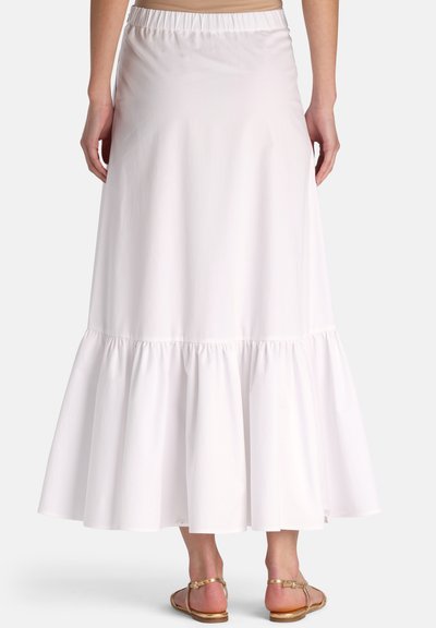 Kvinde iført et hvidt lagdelt midi-nederdel med elastisk taljebånd og gyldne flade sandaler, vist bagfra mod en ensfarvet baggrund.