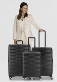 Zwarte bagageset met drie maten. Harde behuizing, gestreept ontwerp, telescopische handgrepen en draaibare wielen voor mobiliteit.