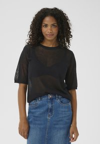 Haut en tricot noir à manches courtes avec une texture transparente et un col rond, associé à une jupe en denim bleue taille haute avec une fermeture à boutons.